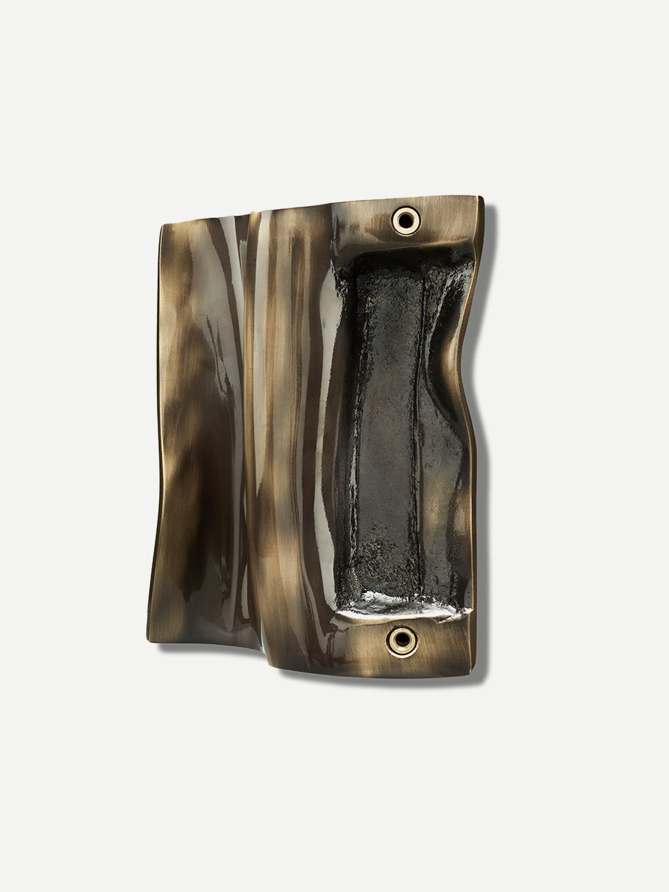 A close-up of the ZEPHYR brass door pull handle in a glossy bronze finish, showcasing its intricate folded brass accents that create a captivating play of light and shadow, perfect for adding a luxurious touch to barn doors, front doors, or sliding doors.