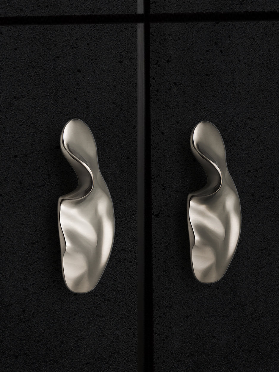 Mockup of artistically shaped cabinet pull in a satin nickel finish installed on a kitchen cabinet, demonstrating its luxurious and creative design.